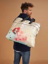 Bolso tote reutilizable de tela Tyvek con estampado abstracto en tonos verdes y negros. Asas de cinta gross negra con inscripción "THOMAS".