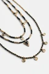 Collar largo múltiple de cuentas doradas y negras con dije triangular central y pequeños dijes colgantes de metal plateado.