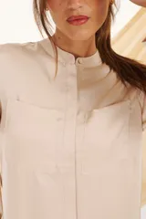 Camisa verde esmeralda de corte recto, cuello mao, cierre frontal con botones y mangas largas con puños abotonados. Presenta dos bolsillos de parche en el pecho.