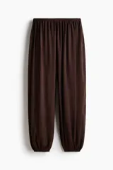 Pantalón baggy de satén color marrón, con cintura elástica y bajos ajustados con elástico, creando un efecto de volumen en las piernas.