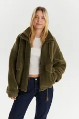 Campera de sherpa color verde musgo, con cuello alto, cierre frontal de cremallera y solapa con botones a presión. Presenta bolsillos delanteros con solapa y cordón de ajuste en el ruedo.