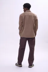 Camisa de pana color tostado, de corte recto y manga larga, con cierre frontal de botones y bolsillo en el pecho.