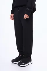 Pantalón deportivo de felpa color negro, con cintura elástica ajustable mediante cordón, puños elásticos en los tobillos y bolsillos laterales.