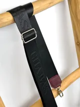 Correa ajustable para cartera confeccionada en cinta tejida con diseño de rayas en negro, blanco y beige, con punteras de cuero sintético negro y herrajes metálicos.