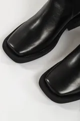 Bota tipo Chelsea de cuero color beige, con paneles laterales elásticos en color negro, puntera cuadrada y suela de goma negra con tacón bajo.