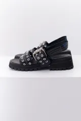 Sandalia de cuero color marrón con suela track negra. Presenta dos tiras frontales con ojalillos metálicos y una tira trasera con cierre de velcro.