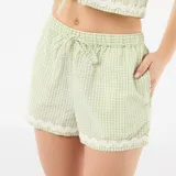 Pijama de dos piezas de cuadros vichy en tonos verde claro y blanco. Incluye una camisa de manga corta con escote en V y cierre frontal mediante lazos, y un short con cintura elástica y cordón ajustable. Ambas prendas cuentan con detalles de ondas bordadas en los bordes.