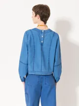 Top de manga larga color azul, confeccionado en denim paper touch. Presenta cuello redondo y recortes en el frente que estilizan la silueta. Tiene cartera en la espalda con broches para facilitar el acceso.