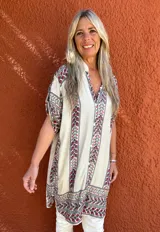 Camisa de seda con fondo crudo y estampado floral multicolor. Presenta cuello camisero, cierre frontal con botones y mangas cortas con diseño holgado.