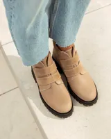 Botín corto de cuero color visón (beige/topo), con cierre de tres tiras de velcro en el empeine. Posee cuello acolchado de gamuza y suela de goma negra con relieve tractor.