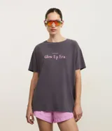 Remera de corte oversized en algodón con efecto desteñido color gris oscuro, cuello redondo, mangas cortas y estampa frontal con la frase "Glow Up Era" en color rosado.