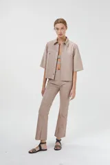 Camisa de cuero ovino color rosa pálido, de corte recto y estilo minimalista. Tiene mangas cortas, cuello clásico, cierre con botones a presión plateados y bolsillos delanteros con solapa.