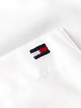 Camisa blanca de manga larga con cuello clásico, bolsillo frontal y logo bordado en el pecho. Presenta detalles distintivos de Tommy Hilfiger en el cuello.