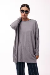 Sweater de silueta amplia y largo medio, con cuello redondo, mangas largas y detalle de botones decorativos en los laterales. Presenta un diseño de tejido de punto con caída relajada.