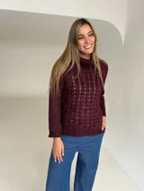 Polera de tejido de punto color bordeaux con cuello semi volcado. Presenta un diseño de ochos en el frente, mientras que las mangas y la espalda son lisas.
