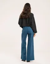 Pantalón de pana color verde oliva, de corte wide leg y largo al tobillo. Tiene cierre delantero con botón, bolsillos laterales y traseros.