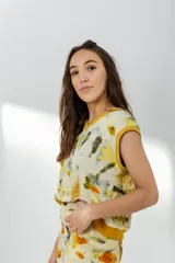 Chaleco de lana merino color crema, con escote en V y diseño sin mangas. Se usa sobre una camisa mostaza de mangas largas con puños elásticos.