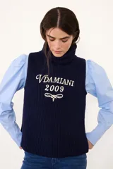 Chaleco de tejido de punto color crema con cuello alto y bordado frontal en color bordó con la inscripción Vdamiani 2009. Presenta detalles de volados en las sisas.