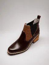Botineta Chelsea de cuero en tono marrón oscuro y tostado, con paneles elásticos negros en los laterales, costuras pespunteadas a contratono y taco cuadrado de madera clara.