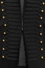Blazer corta de estilo militar en color negro, con cuello redondo, manga larga y hombreras marcadas. Presenta un diseño frontal con bordados decorativos a tono y botones dorados, cierre con gancho metálico y forro interior.