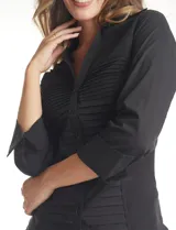 Camisa entallada de color negro con pechera estructurada mediante alforzas horizontales. Presenta cuello con solapa, escote en V, cierre frontal con botones y mangas tres cuartos con puños anchos rebatibles.