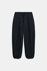 Pantalón de tiro medio, color negro con rayas diplomáticas finas blancas. Cintura elástica ajustable con cordones y bajo abullonado con elástico.