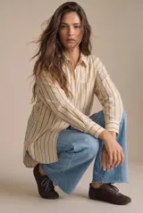 Camisa de corte oversize con estampado de rayas verticales en tonos beige y mostaza. Presenta cuello clásico, cierre frontal con botones, bolsillo aplicado en el pecho y mangas largas con puños abotonados.