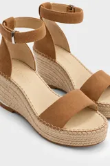 Sandalias de tacón en cuña forrada en yute trenzado, con capellada de cuero negro, tira en el talón y tira ajustable al tobillo con hebilla metálica.