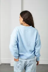 Saco de punto color celeste con cuello en V, cierre frontal con botones y diseño de flores en relieve bordadas sobre la prenda.