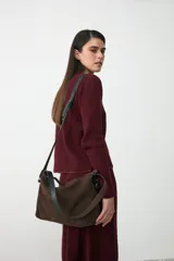 Cartera tipo hobo de gamuza color marrón chocolate, con doble asa: una fija de mano y una correa larga ajustable y extraíble de cuero negro.