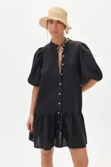 Vestido corto negro de lino con cuello mao, mangas cortas abullonadas, cierre frontal con botones y falda con volantes.