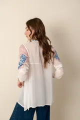 Túnica blanca de seda con bordados florales en azul y rojo, cuello mao con botones y mangas largas.