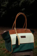 Bolso de fin de semana estilo tote de lona con estampado camuflado, detalles en cuero marrón y gamuza azul, manijas largas y borla decorativa colgante.