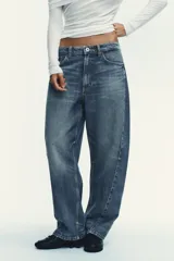 Jeans de tiro medio con diseño baggy barrel, cinco bolsillos y costuras laterales torcidas. Presenta cierre frontal con cremallera y botón metálico.
