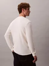 Remera de manga larga Calvin Klein de color blanco off-white, confeccionada en tejido de punto térmico con textura de nido de abeja. Presenta cuello redondo, puños acanalados y un pequeño logo bordado en el pecho.