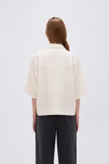 Blusa de lino color natural, con cuello polo y escote en V, de mangas cortas holgadas y corte recto.