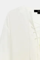 Camisa blanca ZARA Woman Collection de 100% seda, con escote en V ajustable con cordones entrelazados y manga larga con puños rectos.