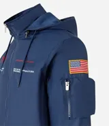 Campera rompevientos azul marino con capucha, cierre frontal y bolsillos laterales. Presenta estampado de NASA en el pecho, parche de bandera estadounidense en la manga y bolsillo utilitario en el brazo.