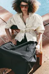 Chaqueta estilo safari color beige, con cuello de solapa tejido en crochet, manga larga, bolsillos delanteros con solapa y cintura ajustable con cordones. Cierre frontal con botones metálicos a presión.