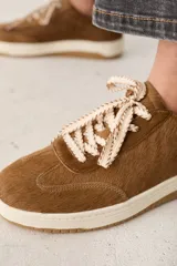 Zapatillas de cuero con textura de pelo, color marrón, con suela de goma color crema y cordones gruesos con diseño trenzado.