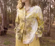 Camisa blanca con estampado de hojas en tonos beige y verde, cuello camisero, mangas largas con lazos en los puños y botones de madera.