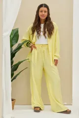 Pantalón de pierna ancha color amarillo pastel, de tiro medio con cintura elástica fruncida y cordón ajustable.