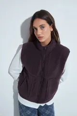 Chaleco de corderito color marrón oscuro, con cierre frontal completo, cuello alto y bolsillos laterales.