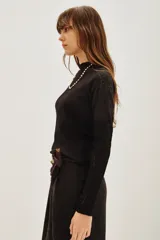 Polera negra de manga larga con diseño combinado, presentando un cuerpo de tejido liso y mangas de encaje con textura. Posee cuello alto y un ajuste entallado al cuerpo.