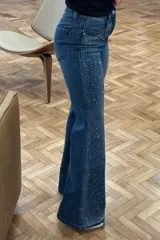 Jeans de denim azul con corte ajustado, cintura media y detalles de strass plateados en la parte superior y los laterales.