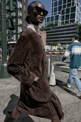 Abrigo marrón de gamuza con cuello redondo, manga larga, bolsillos delanteros y cierre frontal con botones.