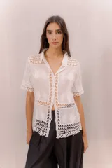 Camisa de algodón color crudo, con cuello camisero, mangas cortas y cierre frontal con botones. Presenta paneles de tejido calado y detalles bordados transparentes.