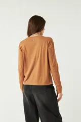 Remera de manga larga color marrón, con cuello redondo y bordado sutil en el pecho izquierdo. Presenta un corte recto con aberturas laterales en el ruedo.