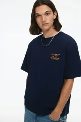 Remera azul marino de corte holgado con cuello redondo y estampado pequeño en el pecho con un avión y texto en color ocre.