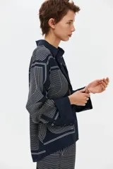 Camisa de sarga de corte oversized, color azul marino, con estampado geométrico de líneas blancas. Presenta cuello clásico, cierre frontal con botones, hombros caídos y mangas largas con puños abotonados.